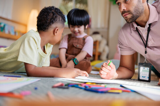 Teacher and children drawing together with crayons on floor.