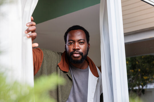 Man looks out window, holding curtain.