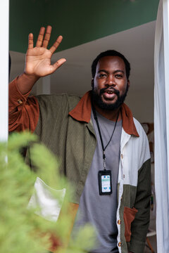 Man waves hello from doorway, wearing name tag.