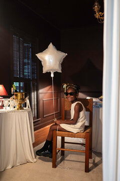 Child Sits on Chair Holding Star Balloon in Indoor Setting