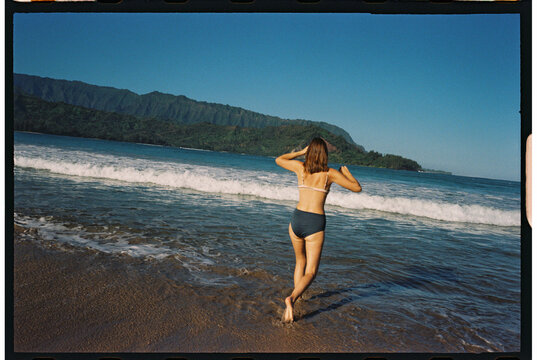 traveler splashing at beach walking into water hanalei bay, kauai 