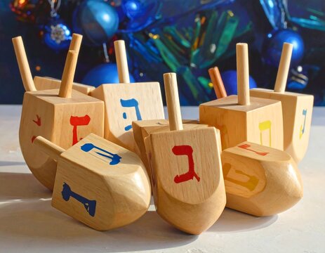 Wooden dreidels with colorful Hebrew letters displayed in front of a blue decorative background for Hanukkah