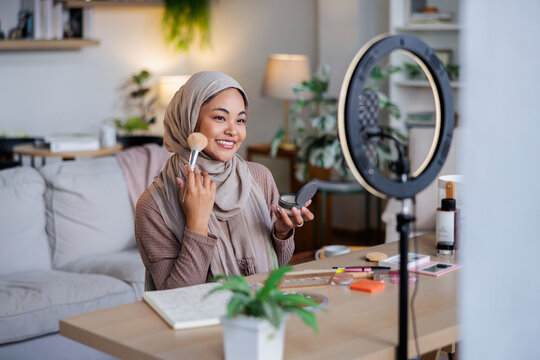 Woman in hijab applies makeup in front of ring light.