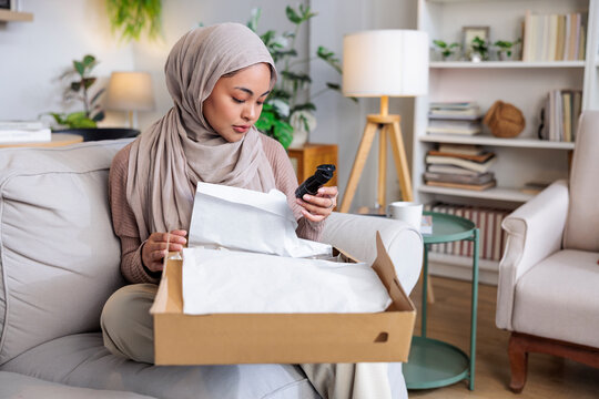 Woman in hijab opens box, examines product.
