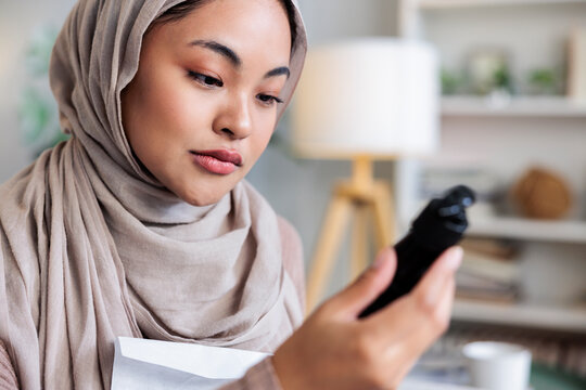 Woman in hijab examines a black object closely.