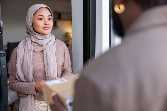 Woman in hijab receives package from delivery person.