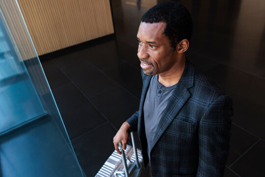 Man with suitcase looks up in modern building.