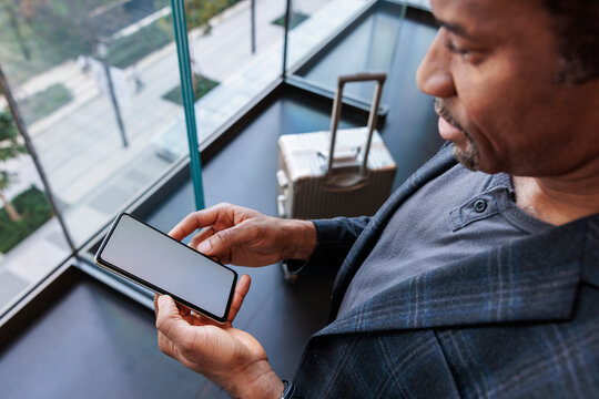 Man with suitcase checks phone near window.