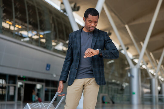 Man checks watch while pulling luggage in airport.