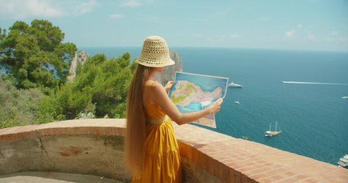Tourist woman reading map above blue sea on Capri viewpoint with view of Faraglioni cliffs
