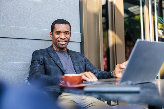 Man works on laptop with coffee outside.