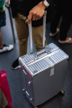 Traveler with silver suitcase and watch in a crowd.