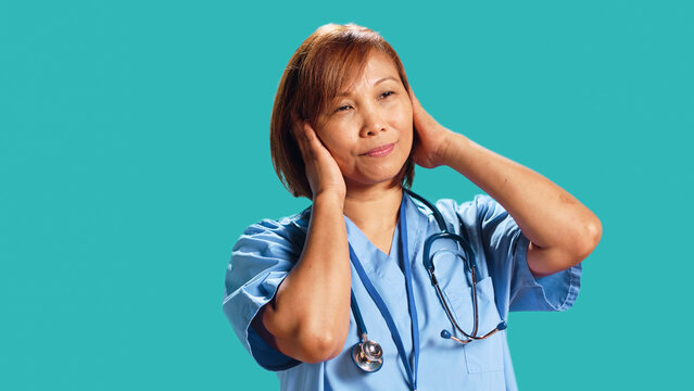 Competent nurse tormented by extreme noise while at work, close up. Healthcare employee covering ears with hands, bothered by rowdy surrounding sounds, isolated over studio background