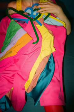 Person Covered with Bright Clothing on Hangers on Blue Background