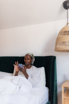Woman Using Smartphone While Sitting on Bed in Simple Room