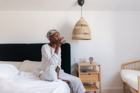 Woman Sitting on Bed Drinking Water in a Cozy Room Setting