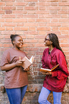 Two friends are smiling near a brick wall.