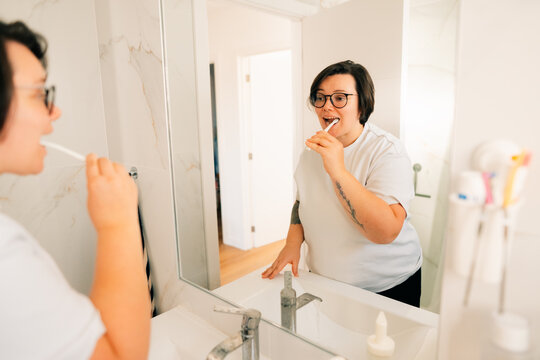 Person Brushing Teeth in Bathroom Mirror in Morning Time