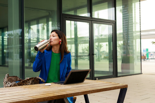 Woman Enjoys Drink While Working on Laptop Outside Building