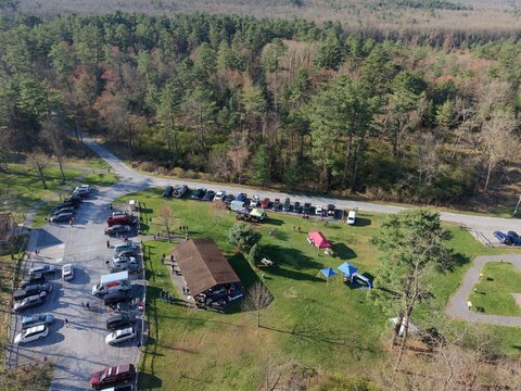 Aerial view of Pine Grove Furnace State Park with a crowded parking lot, a wooden pavilion, and colorful tents nestled against a dense forest Gardners, Pennsylvania, United States.