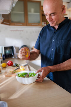 Man squeezes lemon over salad in kitchen.