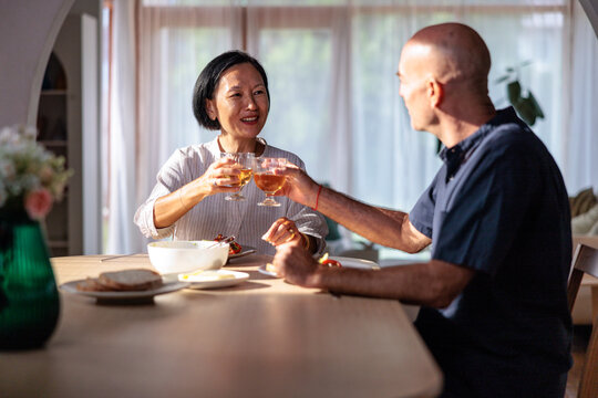 Couple toasting glasses at a table with food.