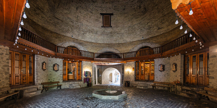 Upper Caravanserai, Shaki, Azerbaijan. Grand circular interior with a domed brick ceiling, wooden balcony, stone walls, cobblestone floor, and central fountain. Historic Silk Road architecture