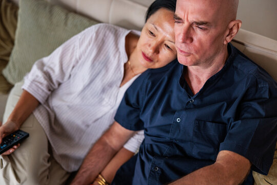 Couple on couch, woman comforting man, both looking down.