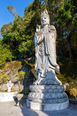 Obraz premium Grand Kuan Yin statue at Chin Swee Caves Temple, Genting Highlands, Pahang, Malaysia. Iconic Buddhist deity, religious landmark against a clear blue sky and lush green trees