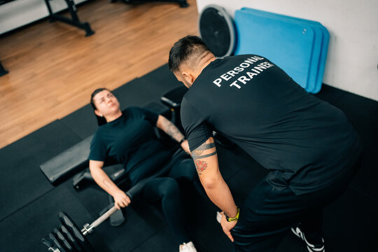 Woman Exercises With Weights in Gym While Trainer Assists