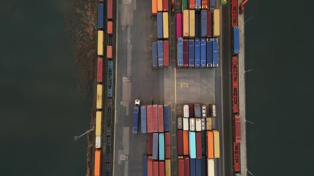 Aerial top down view of a busy container terminal with a reach stacker moving cargo gantry crane loading freight trains and a truck driving through the logistics hub