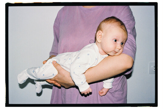 A baby is held in the arms of a parent at home