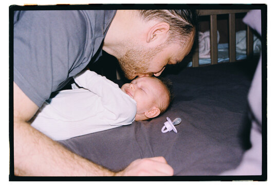 Father kisses baby on bed during evening time