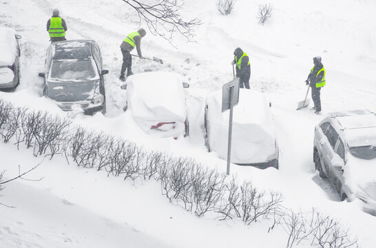 Workers clear snow from cars on a busy street