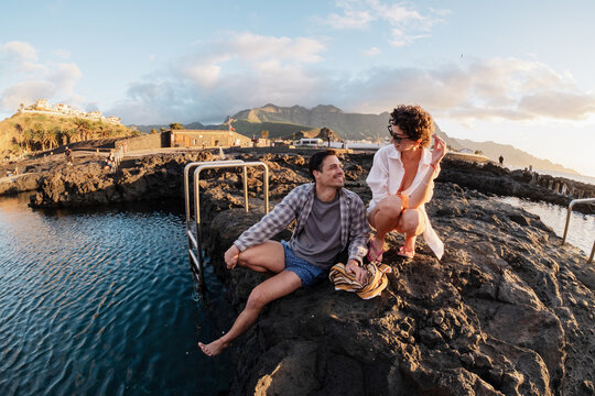 Couple relaxing at natural volcanic rock pools during sunset