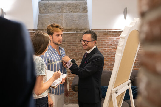 Cheerful tailor measuring client and speaking with assistant