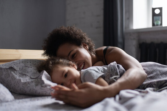 Cheerful black race mother and daughter lying on bed in morning