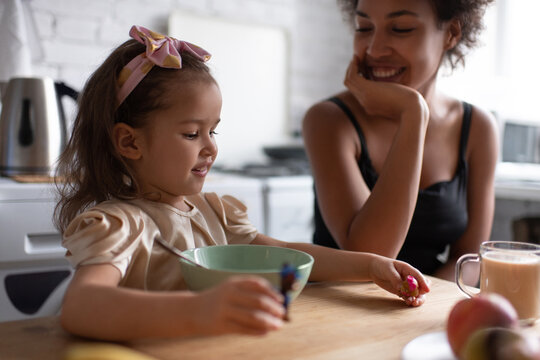 Cheerful multiracial girl playing during breakfast with mother