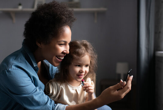 Happy black woman teaching daughter to apply lipstick