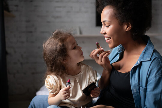 Black Mother teaching multiracial daughter to apply lipstick