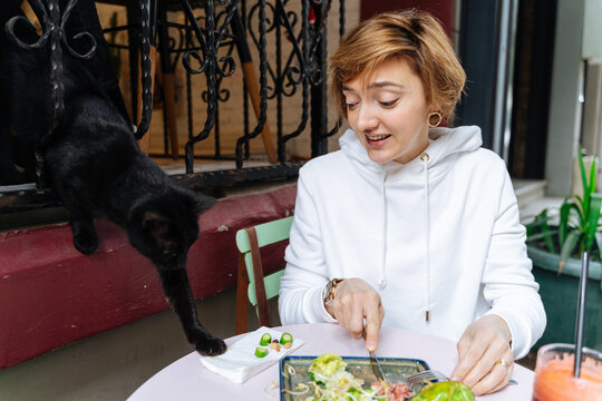 Woman eating at outdoor table with black cat reaching