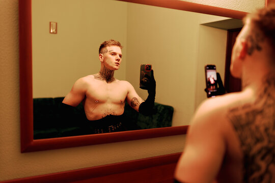 Person Takes Selfie in Mirror While Showing off Tattoos in a Room