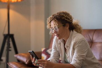 Woman relaxing on couch at home using smartphone and smiling while reading messages