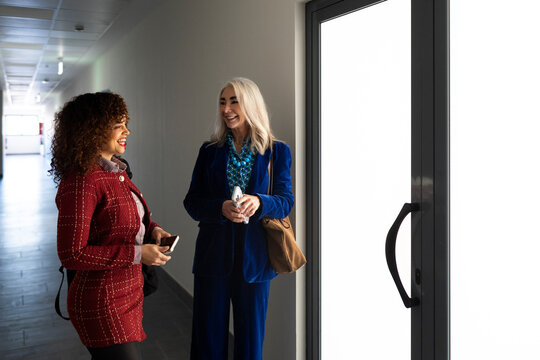 Two businesswomen talking cheerfully  in office hallway 