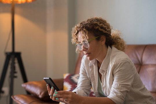 Woman relaxing on couch at home using smartphone and smiling while reading messages