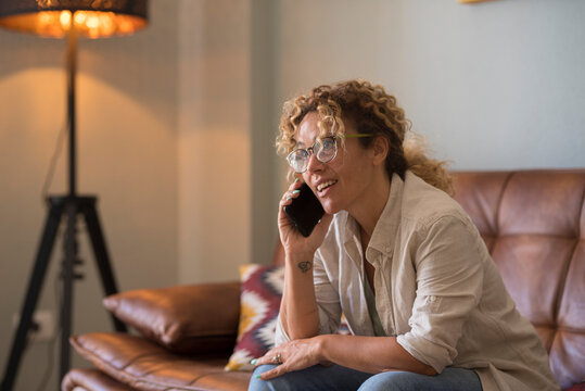 Woman talking on phone and smiling while sitting on a leather couch in a cozy living room