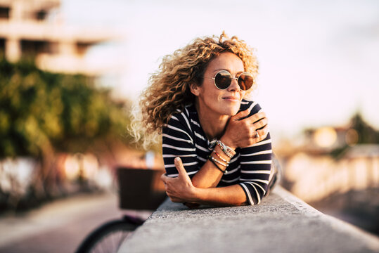 Relaxed woman in sunglasses leaning on a seawall wearing a striped shirt at golden hour
