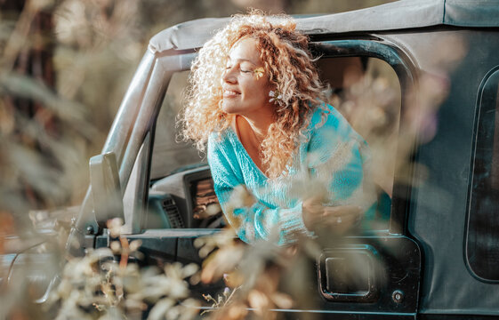 Smiling woman leaning out of car window enjoying sunshine and wildflowers on a relaxed spring drive