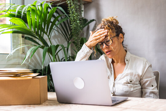 Stressed entrepreneur woman working on laptop at home office with packages and plants