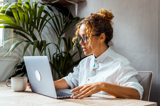 Woman working on laptop in a bright home office, focused remote work and coffee at desk